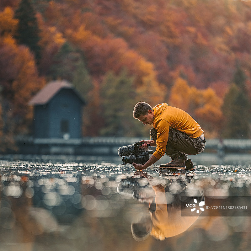男摄影师在自然环境中手持相机在水面上图片素材