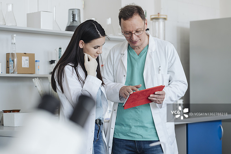 在实验室里，科学家们穿着白色外套，使用平板电脑图片素材