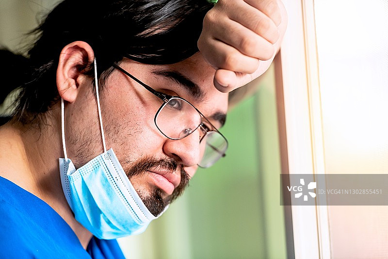 悲伤沉思的年轻西班牙裔医护人员望着窗外图片素材