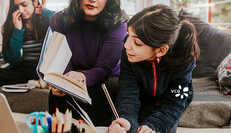 母亲帮助小女儿写作业，大女儿阅读图片素材