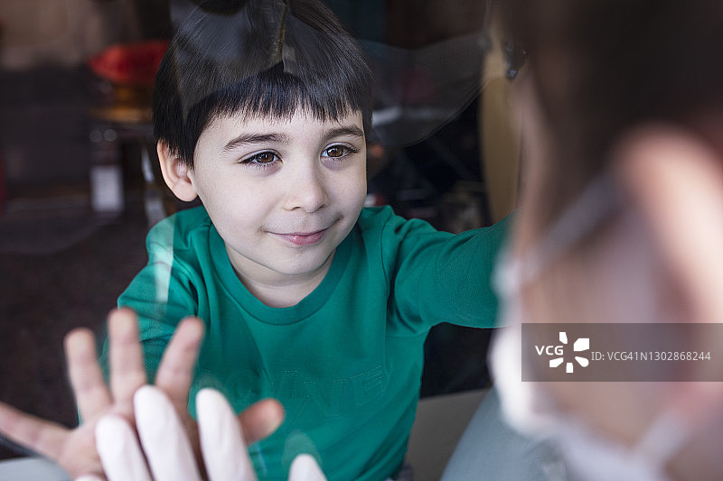 因疫情无法接近母亲的男孩，隔着窗户看着母亲图片素材