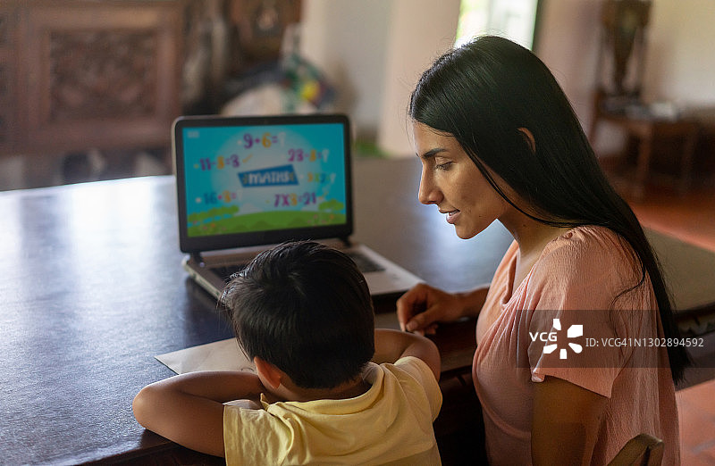 母亲在家里用笔记本电脑监督儿子在线学习图片素材