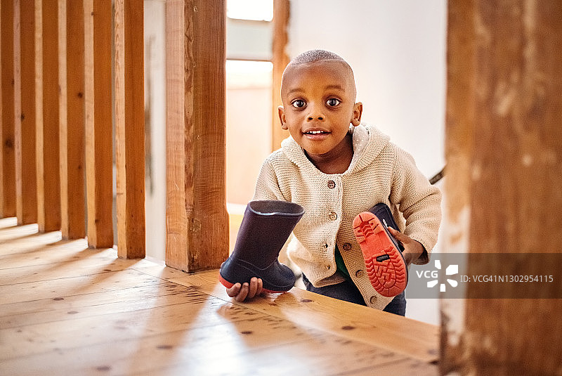 可爱的小男孩拿着橡胶雨靴走上家里的楼梯图片素材