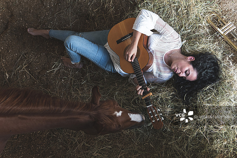 中年女子与马在马厩的干草上弹吉他图片素材