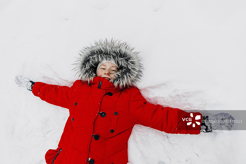 身穿红色保暖服装的女孩在冬季做雪天使图片素材
