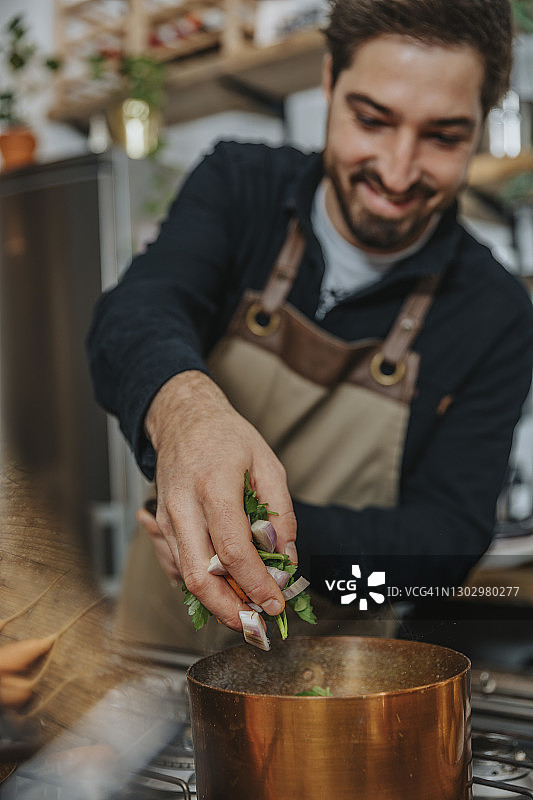 微笑的厨师在厨房里用铜锅放入切碎的蔬菜，制作肉汤图片素材