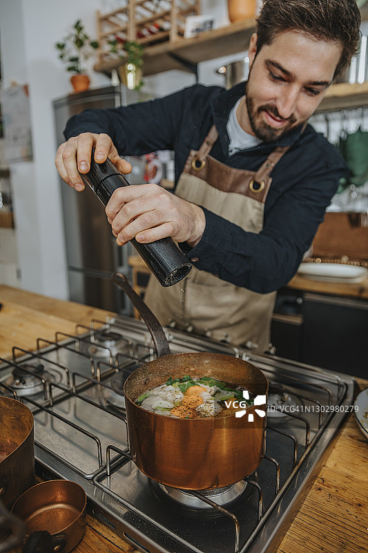专业人士在厨房的铜锅中烹饪肉汤时撒胡椒粉图片素材