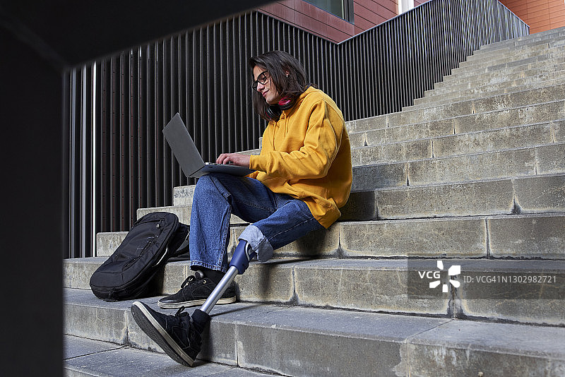 坐在台阶上用笔记本电脑的假肢青年图片素材
