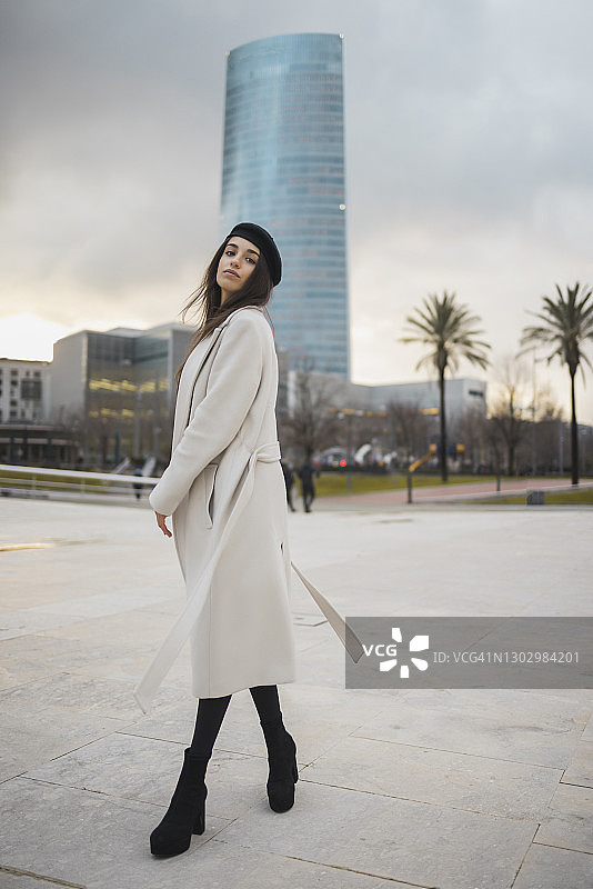 穿着大衣在日落时分的人行道上行走的漂亮女人图片素材