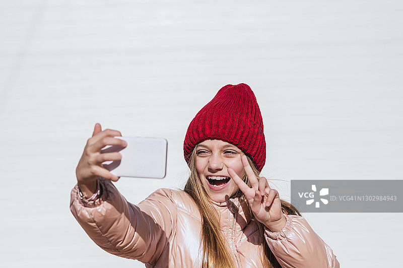 对着白色墙壁用手机自拍的快乐女孩图片素材