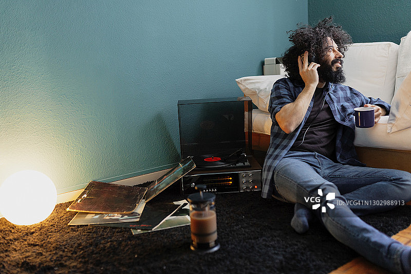 在客厅里一边喝咖啡一边用转盘听音乐的时尚男人图片素材