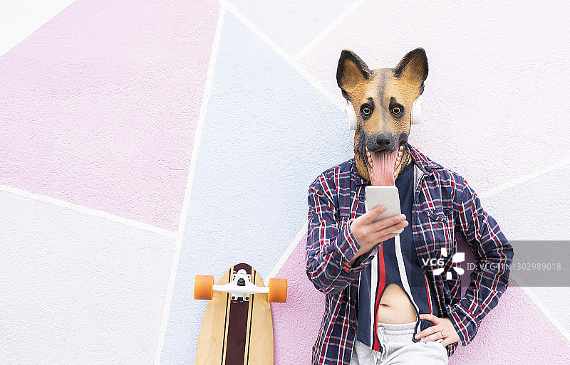 女子戴着狗面具，靠在墙边的滑板旁使用手机图片素材