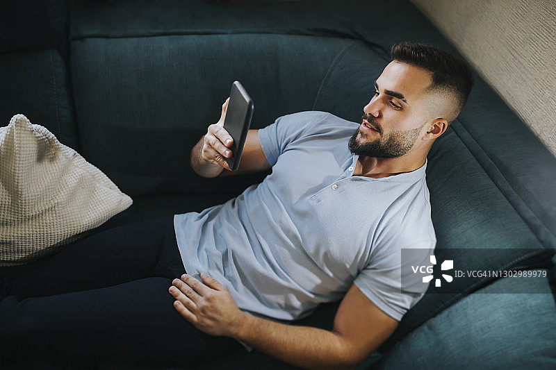 在家躺在沙发上使用智能手机的帅气男人图片素材