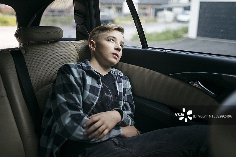坐在汽车后座、透过车窗若有所思的男孩图片素材