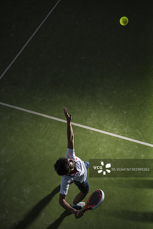 夜晚在运动场上打板式网球的男运动员发球图片素材