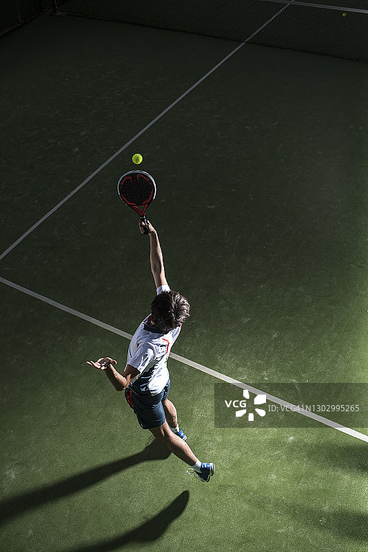 夜晚在运动场上打板式网球的男运动员发球图片素材