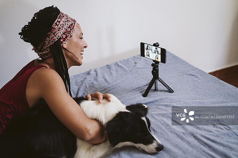 在家中躺在床上与狗通过手机进行视频会议与朋友聊天的微笑女人图片素材
