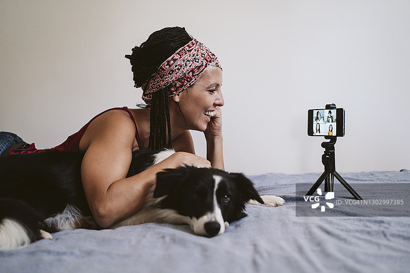 躺在床上，在家里通过手机与朋友交谈的微笑女人图片素材