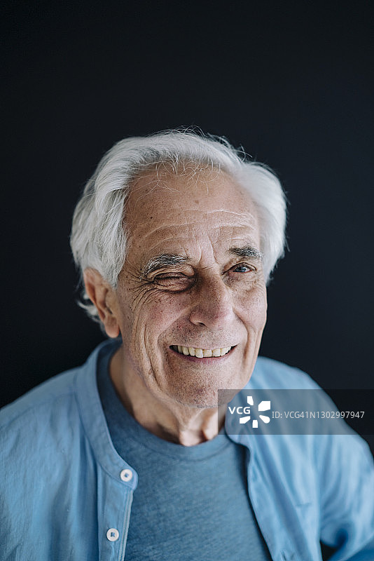 微笑的男人站在黑色背景前眨眼图片素材