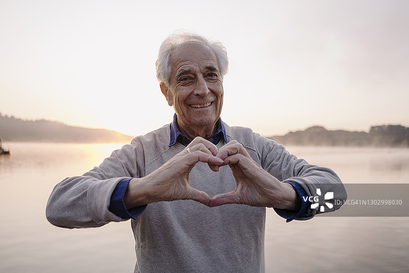 微笑的男人站在湖边用手比心图片素材