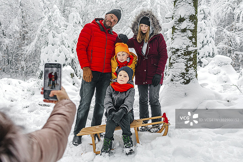 冬天，女人站在森林里用手机给家人拍照图片素材