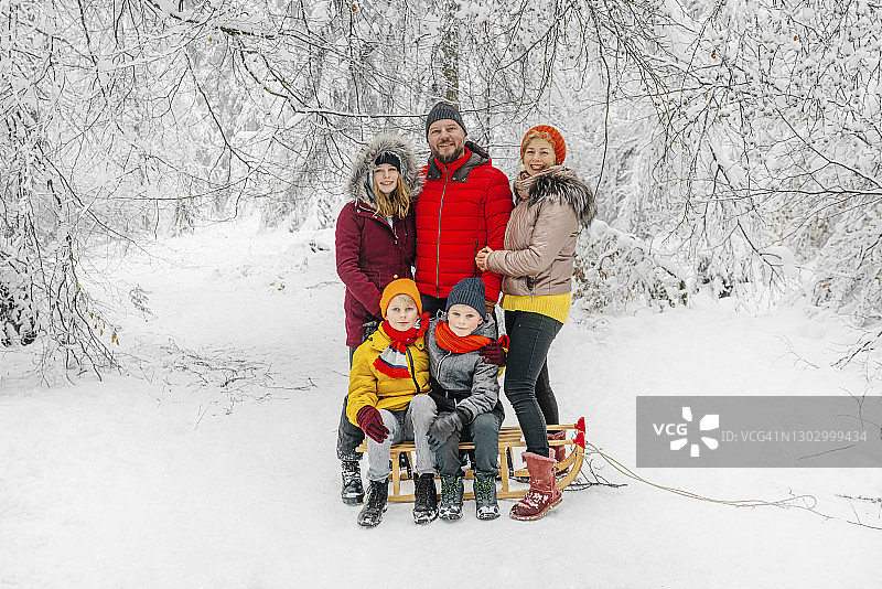 微笑的父母站在坐在雪橇上的孩子旁边图片素材