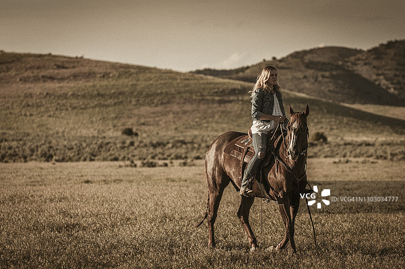 在犹他州，年轻女牛仔在美丽的瓦萨奇山脚下，马匹奔跑前在马背上保持姿势图片素材