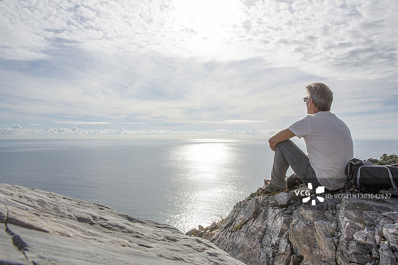 男人坐在海边岩石小丘上眺望远方图片素材