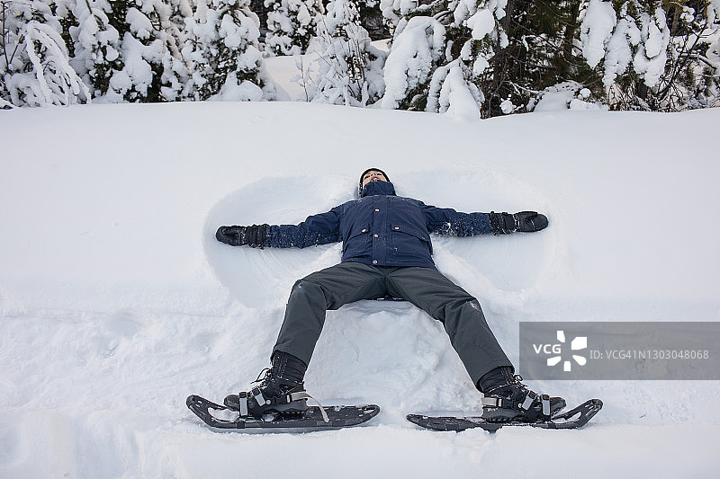 穿着雪鞋的男孩在雪地里制作雪天使图片素材