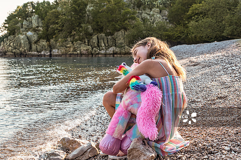 可爱女孩在海滩上抱着她的独角兽玩具图片素材