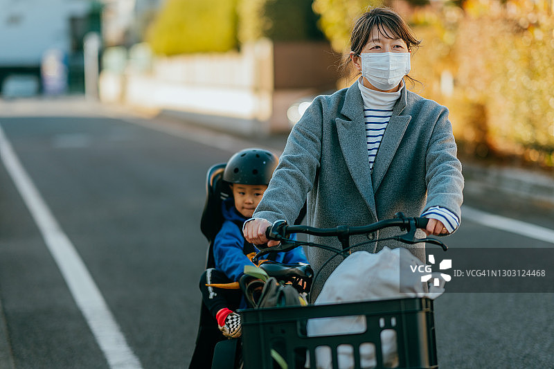 母亲走在街上，推着自行车，儿子坐在自行车后座上图片素材
