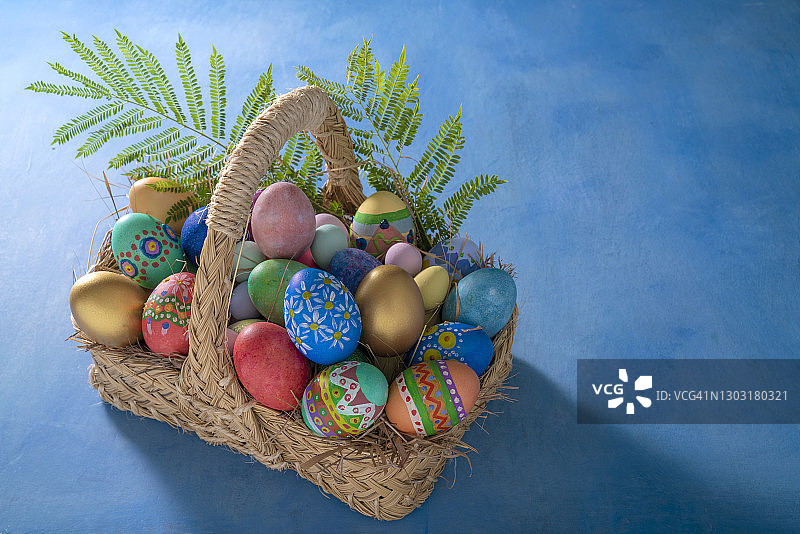 蓝色背景草编篮子里的手绘复活节彩蛋和春草叶图片素材