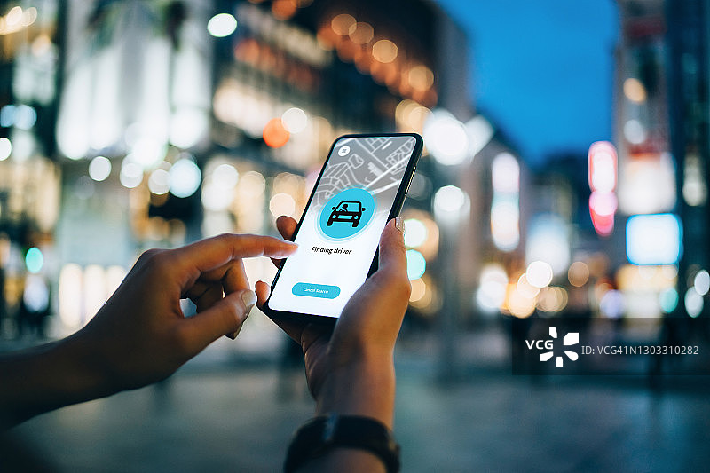 年轻女子在智能手机上使用移动应用程序设备，安排在市中心街道乘坐出租车，背景是灯火通明的城市交通景象图片素材