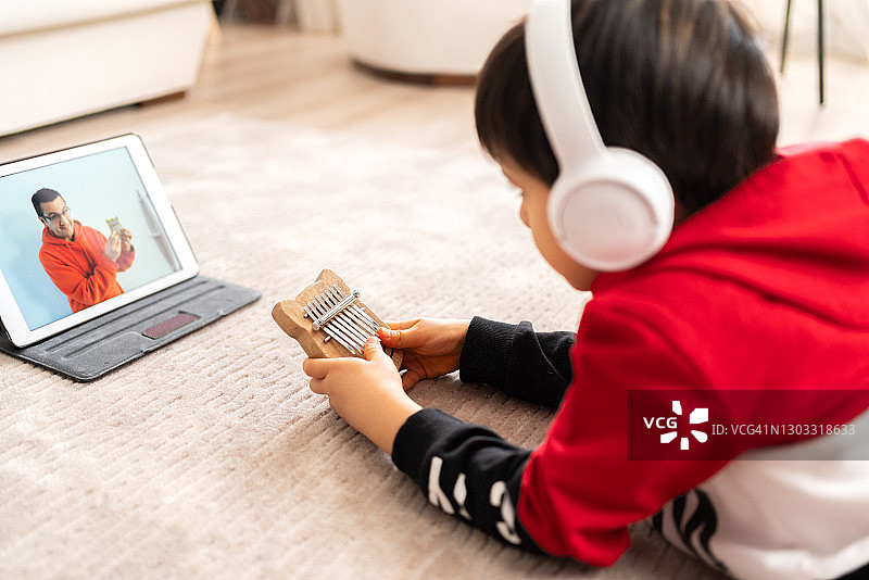 戴着耳机的小男孩通过视频会议系统远程与老师一起演奏卡林巴琴。在线培训，在线课程，远程教育。互联网上有趣的在线课程。居家隔离的现代生活方式图片素材