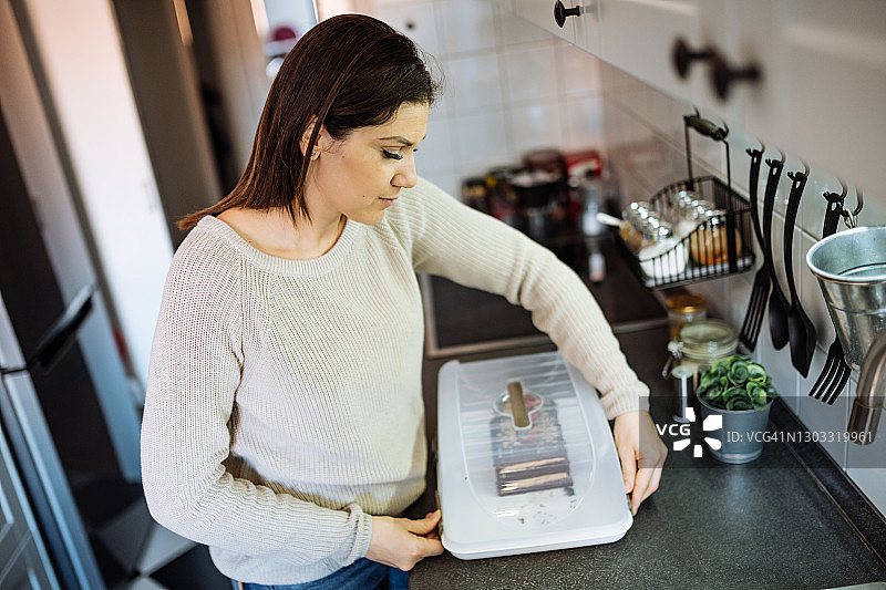 中年女人在厨房里从塑料盒里取出蛋糕图片素材