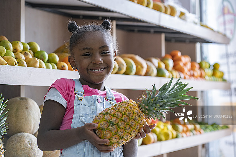 在超市里拿着水果看着镜头的黑人女孩图片素材
