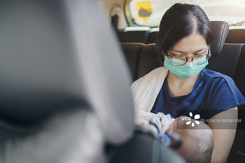 戴着防护口罩的亚洲母亲抱着新生男婴，坐在车内进行母乳喂养图片素材