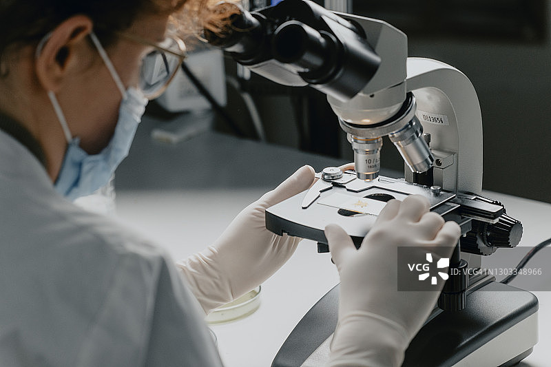 戴着口罩，手持显微镜载玻片的匿名女科学家图片素材