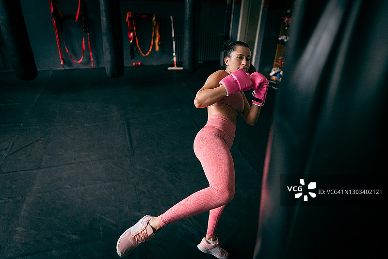 年轻的健身女性在健身房踢重沙袋图片素材