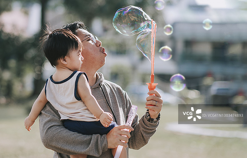 中国亚洲中年男子和他的男婴在公园里玩泡泡图片素材
