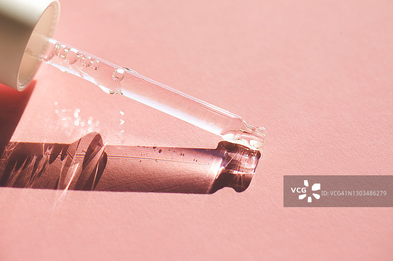 玻璃滴管将透明保湿乳液滴在粉色背景上特写图片素材