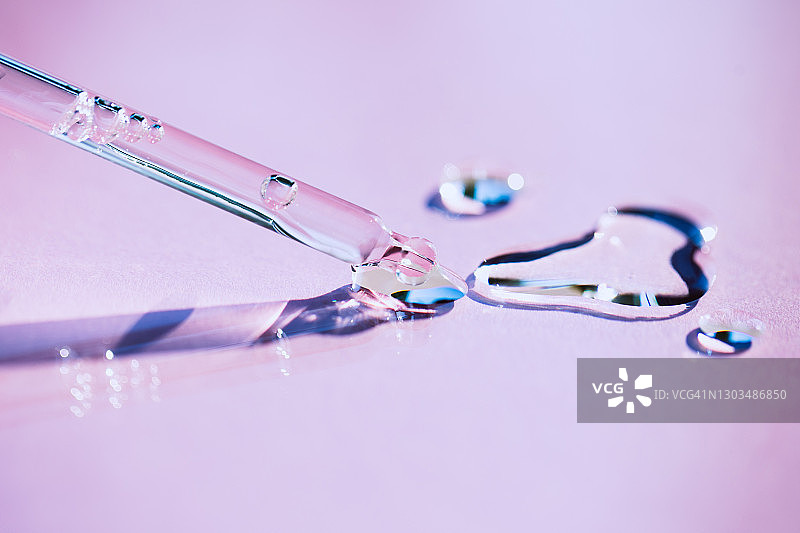 玻璃滴管特写，气泡将透明保湿乳液滴在紫色背景上。年度潮流产品图片素材