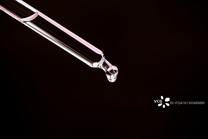 透明清洁保湿乳液从玻璃滴管滴落的特写图片素材