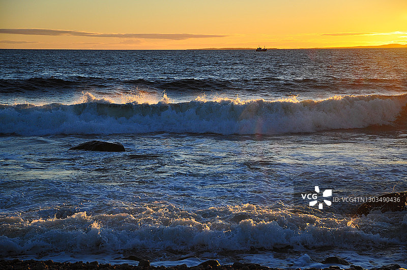 秋日海边日落光中的涌浪，背景是渔船图片素材