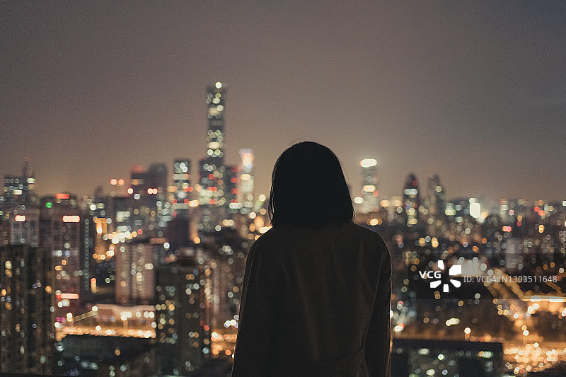 夜晚，女人站立在现代城市前图片素材