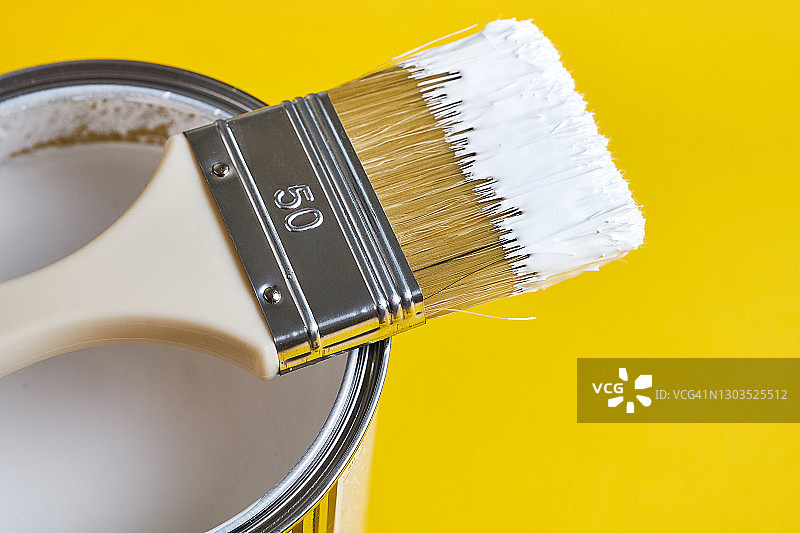 白色油漆罐上的刷子，明亮的黄色背景。绘画和维修工作。创造力、建筑工作、爱好概念图片素材