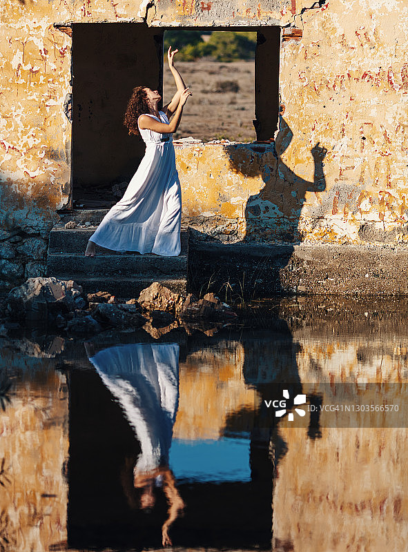 穿着白色长裙站在废弃建筑物前的卷发年轻女人图片素材