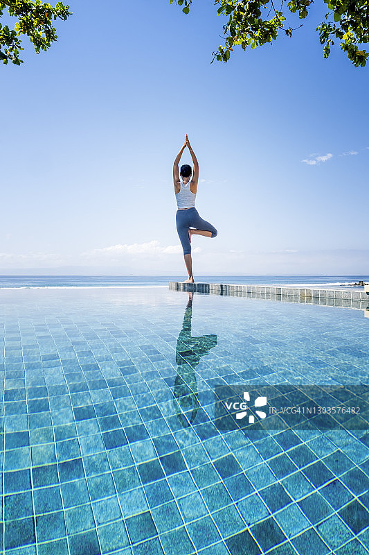 年轻女子在巴厘岛的无边泳池旁练习瑜伽图片素材