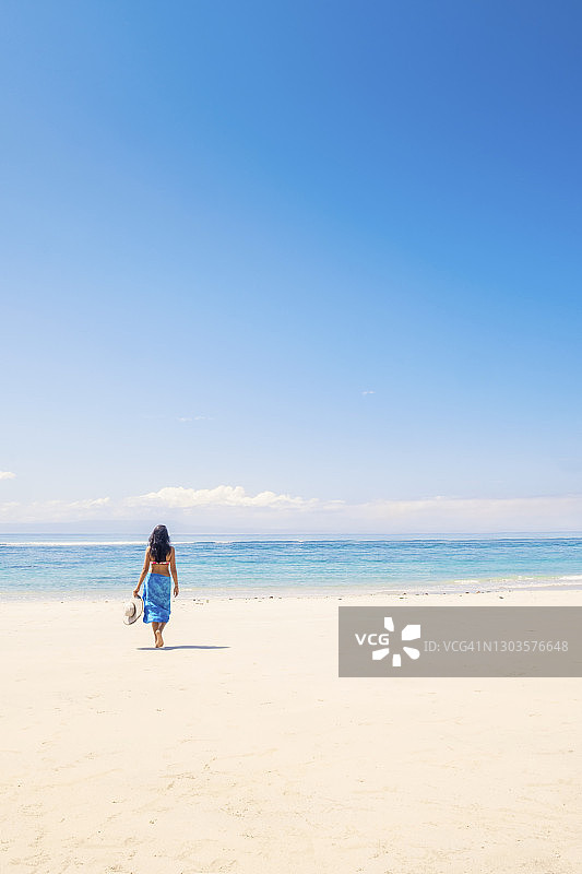 在印度尼西亚热带海滩上手持遮阳帽的深色头发女游客图片素材