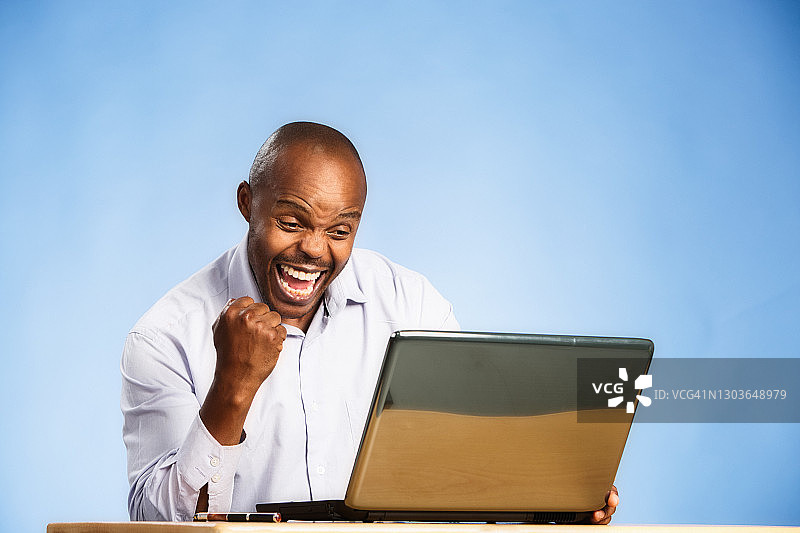 喜悦！英俊男子在使用笔记本电脑时高兴地挥拳图片素材